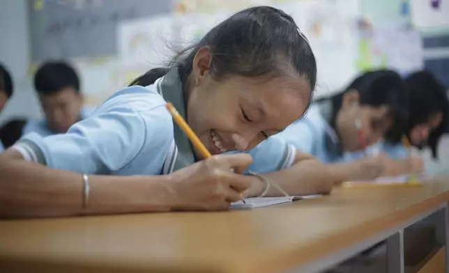 Nguyen Khanh Vy, 19, smiles while writing in her book at a school for victims of Agent Orange in Da Nang, Vietnam, March 7, 2025. (AP Photo/Aniruddha Ghosal)