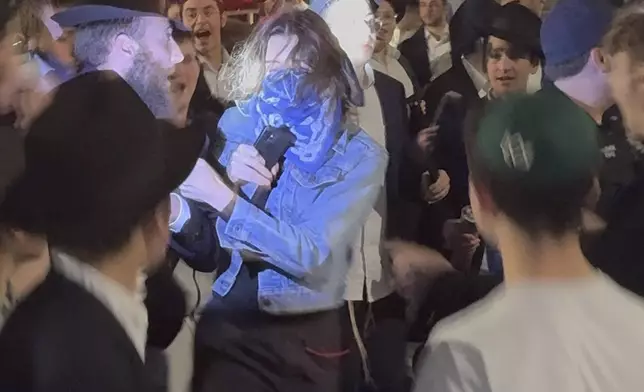 This image taken from video shows a woman and a police officer as they are pursued by a crowd of men in the Crown Heights section of Brooklyn, N.Y., on Thursday, April 24, 2025. (AP Photo)