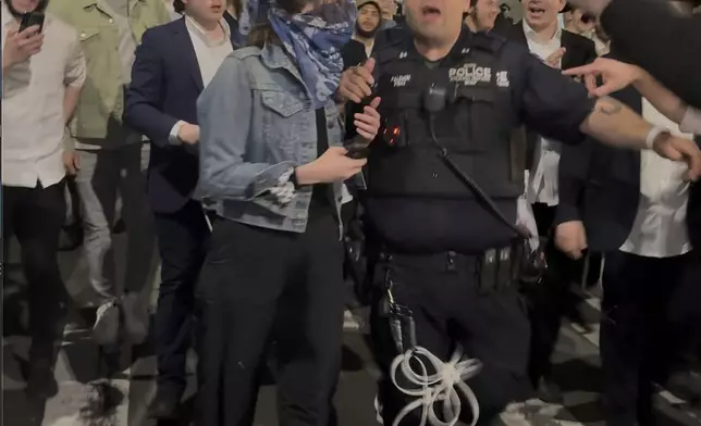 This image taken from video shows a woman and a police officer as they are pursued by a crowd of men in the Crown Heights section of Brooklyn, N.Y., on Thursday, April 24, 2025. (AP Photo)