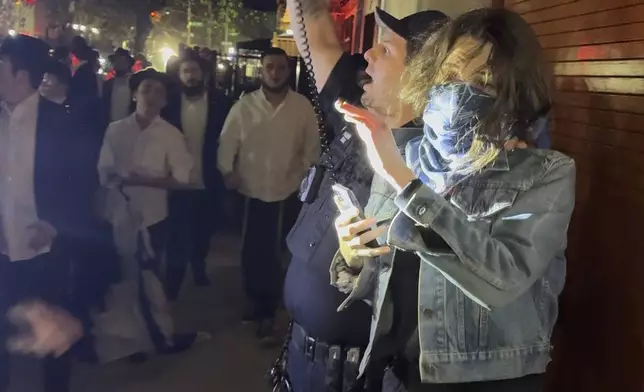 This image taken from video shows a woman and a police officer as they are pursued by a crowd of men in the Crown Heights section of Brooklyn, N.Y., on Thursday, April 24, 2025. (AP Photo)