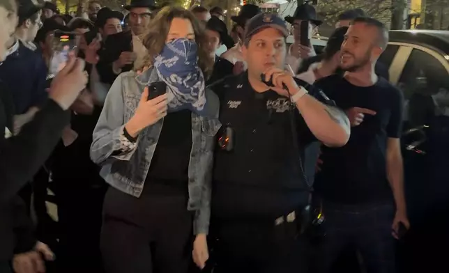 This image taken from video shows a woman and a police officer as they are pursued by a mob of Orthodox Jewish men in the Crown Heights section of Brooklyn, N.Y., on Thursday, April 24, 2025. (AP Photo)