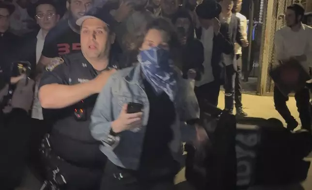 This image taken from video shows a woman and a police officer as they are pursued by a crowd of men in the Crown Heights section of Brooklyn, N.Y., on Thursday, April 24, 2025. (AP Photo)