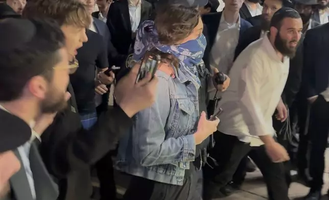 This image taken from video shows a woman and a police officer as they are pursued by a crowd of men in the Crown Heights section of Brooklyn, N.Y., on Thursday, April 24, 2025. (AP Photo)
