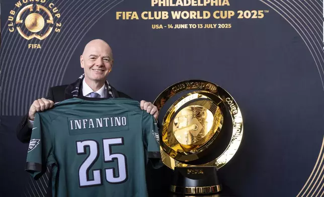 FIFA President Gianni Infantino poses with a Philadelphia Eagles NFL football jersey while next to the trophy at a welcoming event for the 2025 FIFA Club World Cup soccer tournament, Thursday, April 10, 2025, in Philadelphia. (AP Photo/Chris Szagola)