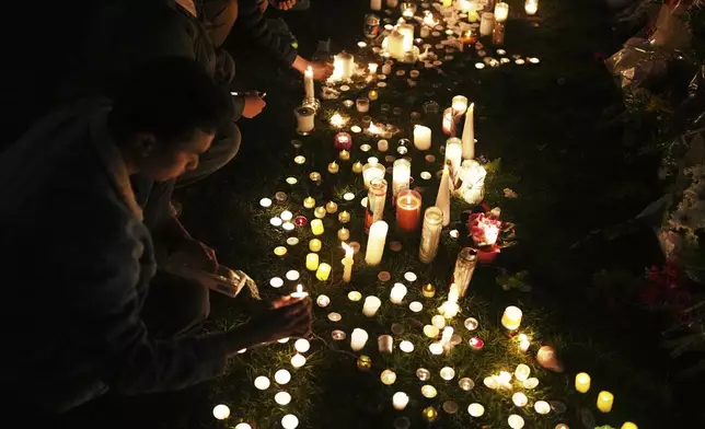 Wendell Gomez, left, places a candle at a memorial for victims after a vehicle drove into a crowd during a Filipino heritage festival in Vancouver, British Columbia, Monday, April 28, 2025. (AP Photo/Lindsey Wasson)