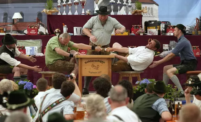 Men dressed in traditional clothes try to pull the opponent over the table at the German Championships in Fingerhakeln or finger wrestling, in Pang, near Rosenheim, Germany, Sunday, April 27, 2025. (AP Photo/Matthias Schrader)