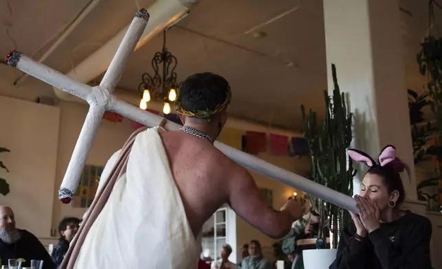 Drag performer Ed Du'Bull, left, holds a cross made to look like lit joints as Krissi Beckel pretends smoke from it during a "blaze and praise" drag brunch at Bar Carlo on Sunday, April 20, 2025, in Portland, Ore. (AP Photo/Jenny Kane)
