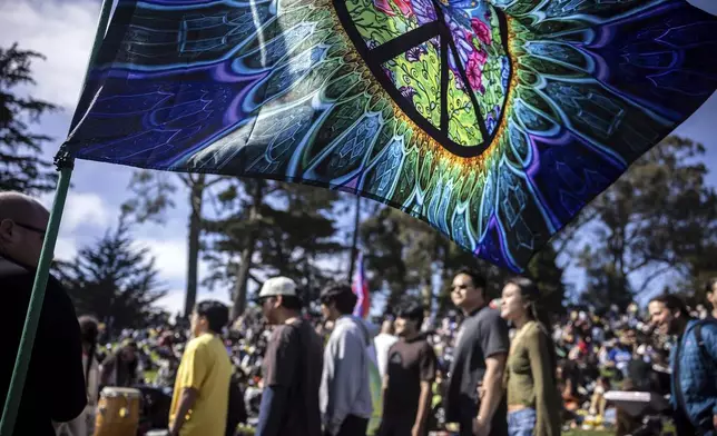 A tie-dyed flag waves as people walk by Hippie Hill where a Volo Sports, "Peace, Love and Volo Sports" event that coincided with Easter gatherings, and an unofficial 420 gathering at Robin Williams Meadow in Golden Gate Park in San Fr, on Sunday, April 20, 2025. (Carlos Avila Gonzalez/San Francisco Chronicle via AP)