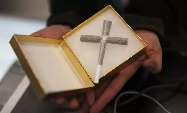 Alexx German displays a joint in the shape of a cross for a customer at Star Buds, a recreational marijuana dispensary, Sunday, April 20, 2025, in Seattle. (AP Photo/Lindsey Wasson)