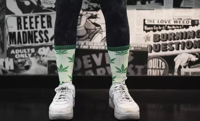 A customer at Have a Heart cannabis dispensary poses for a photo while wearing marijuana-themed leaf socks Sunday, April 20, 2025, in Seattle. (AP Photo/Lindsey Wasson)