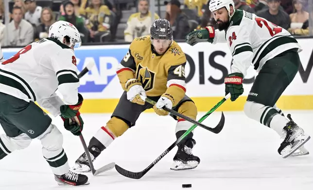 Vegas Golden Knights center Ivan Barbashev (49) skates with the puck against Minnesota Wild defensemen Zeev Buium (8) and Zach Bogosian (24) during the second period of Game 2 of a first-round NHL hockey playoff series Tuesday, April 22, 2025, in Las Vegas. (AP Photo/David Becker)