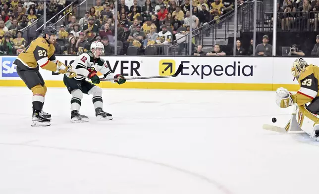 Minnesota Wild left wing Matt Boldy (12) shoots against Vegas Golden Knights goaltender Adin Hill (33) as defenseman Shea Theodore (27) defends during the first period of Game 2 of a first-round NHL hockey playoff series Tuesday, April 22, 2025, in Las Vegas. (AP Photo/David Becker)
