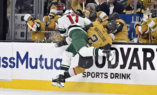 Minnesota Wild left wing Marcus Foligno (17) checks Vegas Golden Knights defenseman Zach Whitecloud (2) into the boards during the first period of Game 2 of a first-round NHL hockey playoff series Tuesday, April 22, 2025, in Las Vegas. (AP Photo/David Becker)
