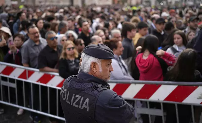 A policeman stands next to people waiting to enter St. Peter's Square to pay their respects to the late Pope Francis, lying in state at St. Peter's Basilica for the final day, at the Vatican, Friday, April 25, 2025. (AP Photo/Andreea Alexandru)