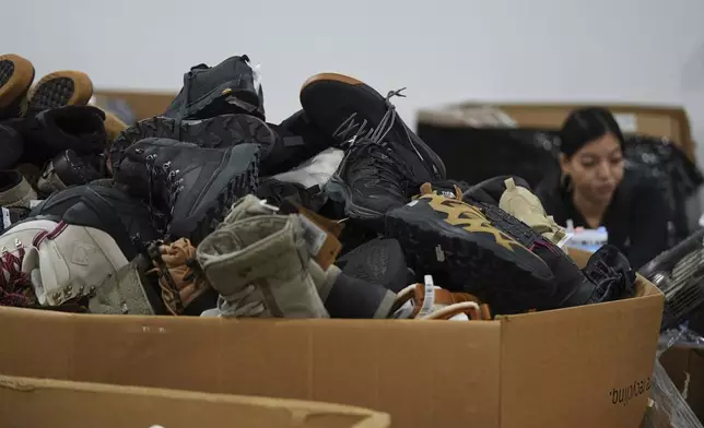 People work amid boxes of returned or overstocked clothing, shoes, boots, coats, packs and other items in a warehouse where the goods are cleaned or repaired before they are marketed on resale platforms in Englewood, Colo., on Thursday, April 17, 2025. (AP Photo/David Zalubowski)