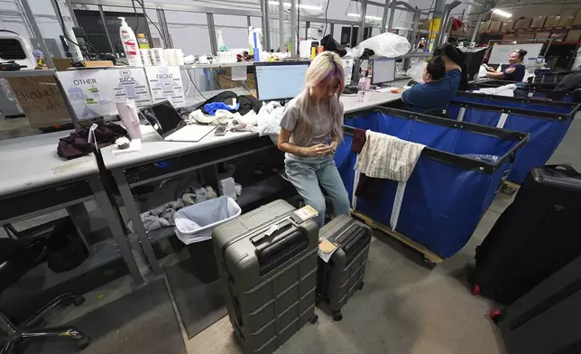 A woman works amid boxes of returned or overstocked clothing, shoes, boots, coats, packs and other items in a warehouse where the goods are cleaned or repaired before they are marketed on resale platforms in Englewood, Colo., on Thursday, April 17, 2025. (AP Photo/David Zalubowski)