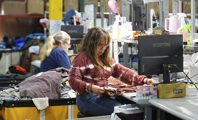 People work amid boxes of returned or overstocked clothing, shoes, boots, coats, packs and other items in a warehouse where the goods are cleaned or repaired before they are marketed on resale platforms in Englewood, Colo., on Thursday, April 17, 2025. (AP Photo/David Zalubowski)