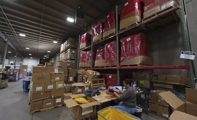 People work amid boxes of returned or overstocked clothing, shoes, boots, coats, packs and other items in a warehouse where the goods are cleaned or repaired before they are marketed on resale platforms in Englewood, Colo., on Thursday, April 17, 2025. (AP Photo/David Zalubowski)