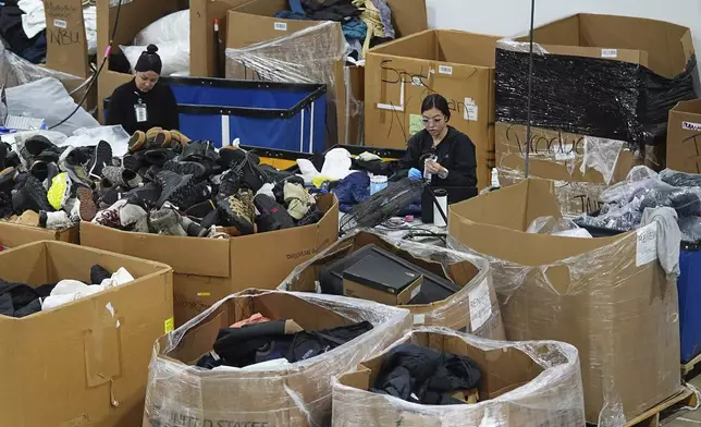 People work amid boxes of returned or overstocked clothing, shoes, boots, coats, packs and other items in a warehouse where the goods are cleaned or repaired before they are marketed on resale platforms in Englewood, Colo., on Thursday, April 17, 2025. (AP Photo/David Zalubowski)