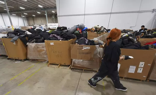 A worker walks past boxes of returned or overstocked clothing, shoes, boots, coats, packs and other items in a warehouse where the goods are cleaned or repaired before they are marketed on resale platforms in Englewood, Colo., on Thursday, April 17, 2025. (AP Photo/David Zalubowski)