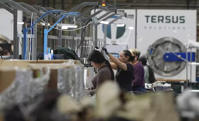 People work amid boxes of returned or overstocked clothing, shoes, boots, coats, packs and other items in a warehouse where the goods are cleaned or repaired before they are marketed on resale platforms in Englewood, Colo., on Thursday, April 17, 2025. (AP Photo/David Zalubowski)