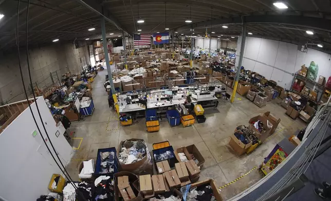Seen through a fisheye lens, people work amid boxes of returned or overstocked clothing, shoes, boots, coats, packs and other items in a warehouse where the goods are cleaned or repaired before they are marketed on resale platforms in Englewood, Colo., on Thursday, April 17, 2025. (AP Photo/David Zalubowski)