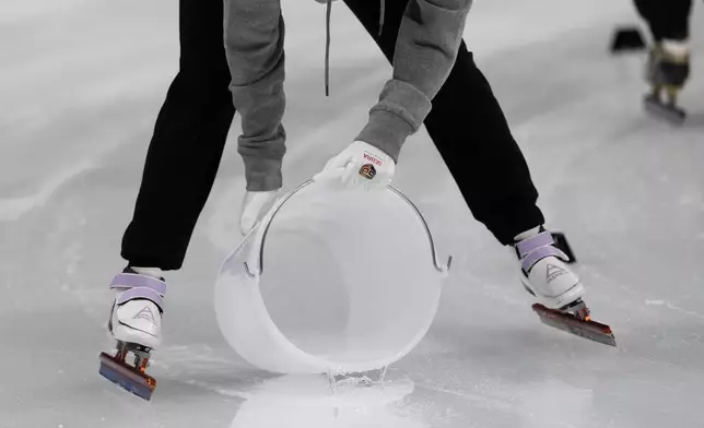 An insider spits out a bucket of water on the track during preliminaries round of the ISU Short Track World Tour, Milan Cortina 2026 Winter Olympics test event, in Milan, Italy, Friday, Feb. 14, 2025. (AP Photo/Luca Bruno)