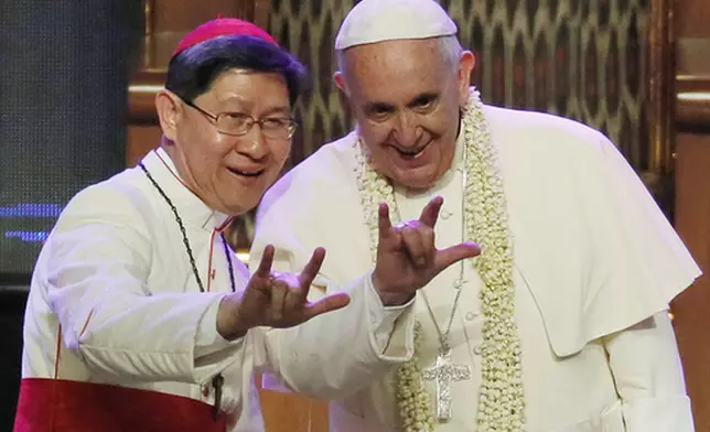 FILE - Filipino Cardinal Luis Antonio Tagle, left, shows Pope Francis how to give the popular hand sign for "I love you" at the Mall of Asia arena in Manila, Philippines, Friday, Jan. 16, 2015. (AP Photo/Wally Santana, File)