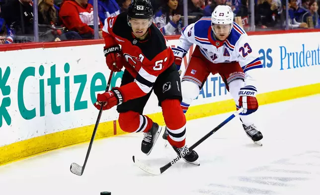 New Jersey Devils left wing Jesper Bratt (63) plays the puck away from New York Rangers defenseman Adam Fox (23) during the second period of an NHL hockey game, Saturday, April 5, 2025, in Newark, N.J. (AP Photo/Noah K. Murray)