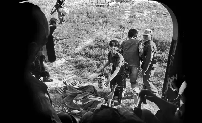 FILE- As her wounded husband raises his arm, a Vietnamese woman begs to be taken aboard a U.S. evacuation helicopter so they can escape a Viet Cong attack in Ba Gia, July 1965. The couple was left behind. (AP Photo/Eddie Adams, File)