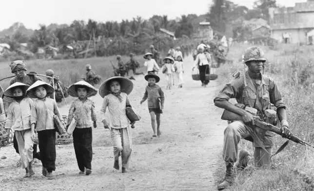 FILE- In an area heavily infiltrated by Viet Cong, a U.S. 1st Division soldier guards Route 7 as Vietnamese market women and schoolchildren return home to the village of Xuan Dien from Ben Cat, December 1965. (AP Photo/Horst Faas, File)