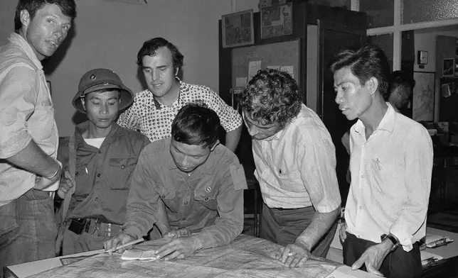 The last three staffers in The Associated Press' Saigon bureau, reporters Matt Franjola, left, Peter Arnett, rear, and George Esper, second from right, are joined by two North Vietnamese soldiers and a member of the Viet Cong on the day the government of South Vietnam surrendered, April 30, 1975. One of the soldiers is showing Esper the route of his final advance into the city. (AP Photo/Sarah Errington)