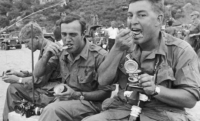 AP correspondent Peter Arnett and AP staff photographer Horst Faas eat while waiting for the arrival of the U.S. 1st Division in July 1965 in Cam Ranh Bay. Faas eats a French-made sausage sauerkraut meal from a can while Arnett has a C-ration. (AP Photo/AP Corporate Archives)