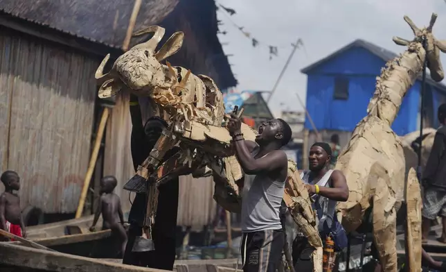 Puppeteers move cardboard animals in canoes at the Makoko Slum in Lagos Nigeria, Saturday, April 19, 2025, as part of "The Herds," a moving theatre performance that started its journey from the Democratic Republic of the Congo to the Arctic Circle in a bid to bring attention to the climate crisis. (AP Photo/Sunday Alamba)