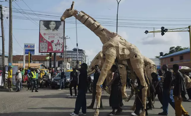 Puppeteers move cardboard animals on the street of Lagos Nigeria, Saturday, April 19, 2025, as part of "The Herds," a moving theatre performance that started its journey from the Democratic Republic of the Congo to the Arctic Circle in a bid to bring attention to the climate crisis. (AP Photo/Sunday Alamba)