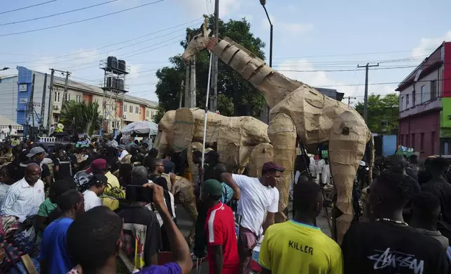 Puppeteers move cardboard animals on the street of Lagos Nigeria, Saturday, April 19, 2025, as part of "The Herds," a moving theatre performance that started its journey from the Democratic Republic of the Congo to the Arctic Circle in a bid to bring attention to the climate crisis. (AP Photo/Sunday Alamba)
