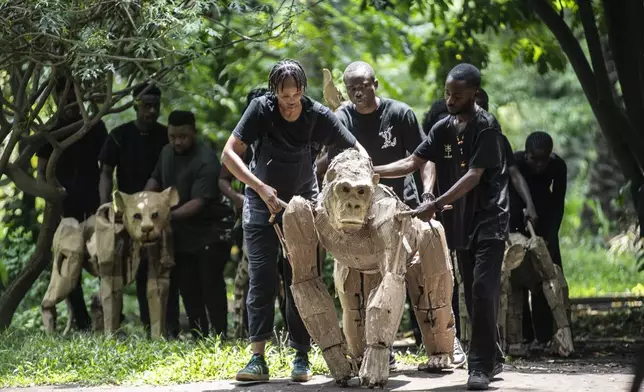 Puppeteers move cardboard animals through DRC's capital Kinshasa's botanical gardens Thursday, April 10, 2025, the first steps of "The Herds", a moving theatre performance that will travel from the Democratic Republic of the Congo to the Arctic Circle in a bid to bring attention to the climate crisis. (AP Photo/Samy Ntumba Shambuyi)