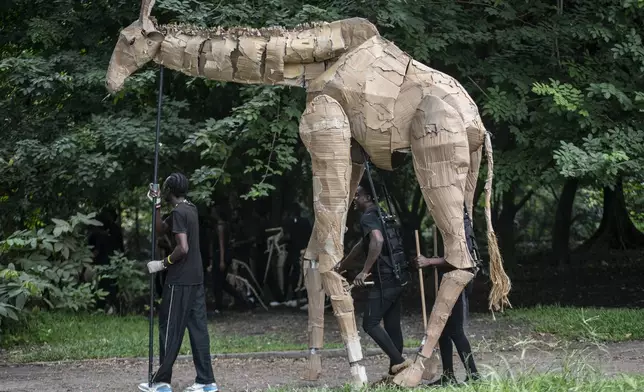 Puppeteers move cardboard animals through DRC's capital Kinshasa's botanical gardens Thursday, April 10, 2025, the first steps of "The Herds", a moving theatre performance that will travel from the Democratic Republic of the Congo to the Arctic Circle in a bid to bring attention to the climate crisis. (AP Photo/Samy Ntumba Shambuyi)