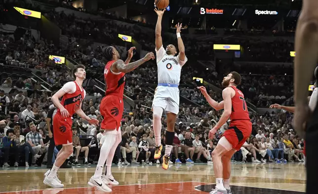 San Antonio Spurs guard Keldon Johnson (0) shoots against Toronto Raptors guard A.J. Lawson, second from left, during the first half of an NBA basketball game, Sunday, April 13, 2025, in San Antonio. (AP Photo/Darren Abate)