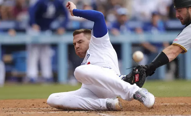 Los Angeles Dodgers' Freddie Freeman, left, slides into home plate to score ahead of a tag during the first inning of a baseball game against the Pittsburgh Pirates in Los Angeles, Sunday, April 27, 2025. (AP Photo/Jessie Alcheh)