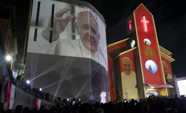 Photos of late Pope Francis are projected outside Saint George Church on the feast day of Saint George in Rio de Janeiro, before sunrise, Wednesday, April 23, 2025. (AP Photo/Bruna Prado)