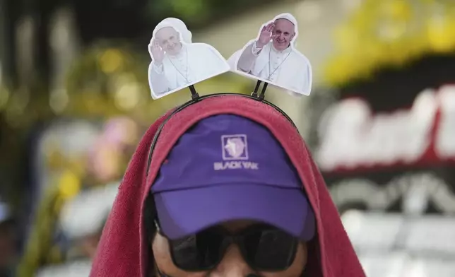 A vendor wears a head accessories of Pope Francis outside the Apostolic Nunciature in Jakarta, Indonesia, Thursday, April 24, 2025. (AP Photo/Dita Alangkara)