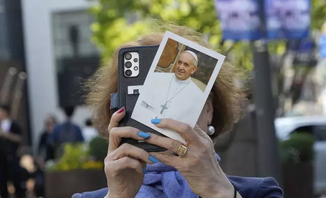 South Korean Kim Seung-hoe with a portrait of the late Pope Francis takes photos outside Myeongdong Cathedral in Seoul, South Korea, Wednesday, April 23, 2025. (AP Photo/Ahn Young-joon)