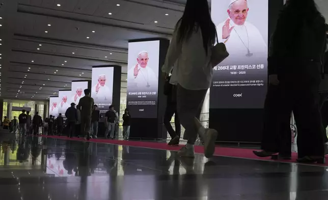 People walk past near the screens showing the portraits of the late Pope Francis at the Coex in Seoul, South Korea, Thursday, April 24, 2025. (AP Photo/Lee Jin-man)