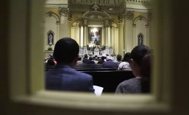 Parishioners, as seen through a window, partake in a prayer service in remembrance of Pope Francis at St. Ignatius Catholic Church, Tuesday, April 22, 2025, in Baltimore. (AP Photo/Stephanie Scarbrough)