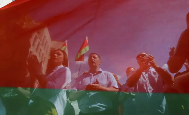 FILE – Belarusian government supporters, seen through a state flag, listen to a speaker at a rally at Independence Square in Minsk, Belarus, on Aug. 16, 2020. (AP Photo, File)