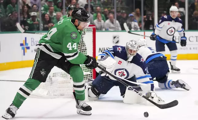 Winnipeg Jets goaltender Connor Hellebuyck, center, eyes the puck as Dallas Stars defenseman Cody Ceci (44) attacks during the first period of an NHL hockey game Thursday, April 10, 2025, in Dallas. (AP Photo/Julio Cortez)