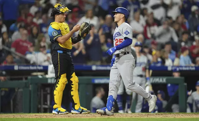 Los Angeles Dodgers' Tommy Edman, right, scores past Philadelphia Phillies catcher J.T. Realmuto, left, after hitting a two-run home run off pitcher Jordan Romano of during the ninth inning of a baseball game, Friday, April 4, 2025, in Philadelphia. (AP Photo/Matt Rourke)