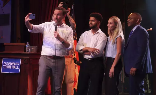 Sen. Chris Murphy, D-Conn., holds a phone as he, Rep. Maxwell Frost, D-Fla., with folded arms, and others, record a message to a Republican lawmaker during a Democratic town hall at the Haw River Ball Room in Saxapahaw, N.C., Thursday, April 24, 2025. (AP Photo/Allen G. Breed)