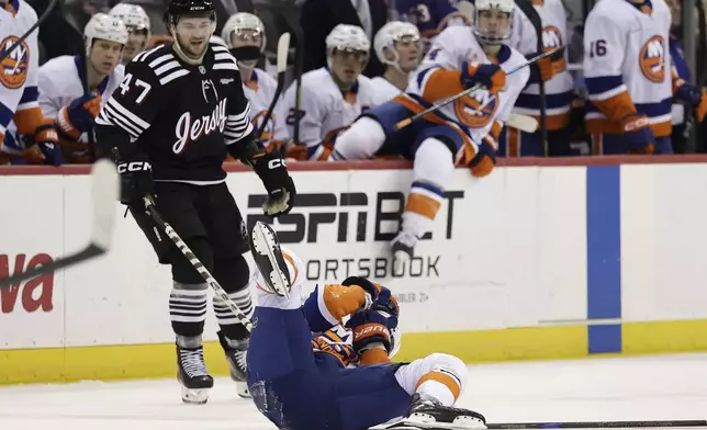 New York Islanders defenseman Adam Pelech (3) lays on the ice after being hit by New Jersey Devils center Paul Cotter (47) in the second period of an NHL hockey game Sunday, April 13, 2025, in Newark, N.J. (AP Photo/Adam Hunger)